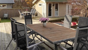 Un terrazzo in legno con mobili da esterno, un piccolo deposito e un'area giardino.