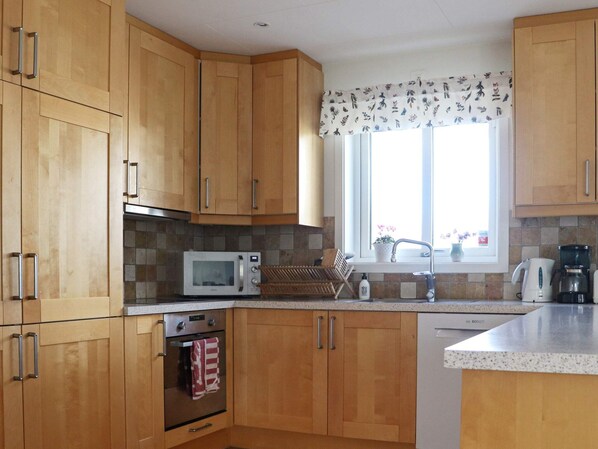 A kitchen with wooden cabinets, a microwave, an oven, a sink, and a window with a floral curtain.