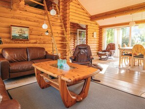 A log cabin interior with a leather sofa, a wooden coffee table, and a dining area with wooden chairs.