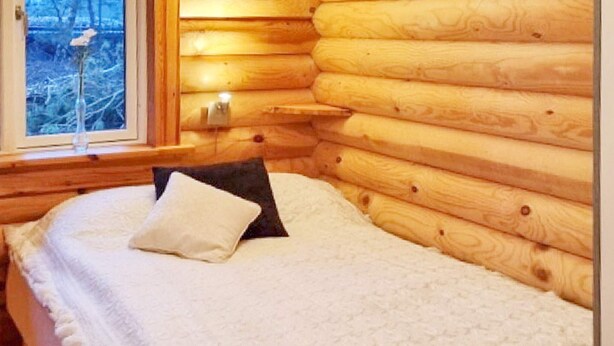 Une chambre dans un chalet en rondins, avec un lit, des oreillers et une fenêtre donnant sur un paysage agréable.