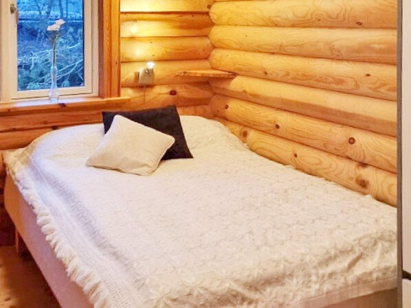 A log cabin bedroom with a bed, pillows, and a window with a view.
