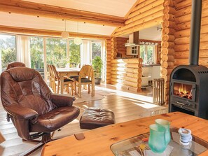 A log cabin interior with a leather sofa, dining table, and a wood-burning stove. - 7 Person Holiday Home in Hadsund (Hadsund)