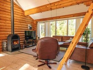 A log cabin interior with a fireplace, a leather sofa, a television, and a large window.