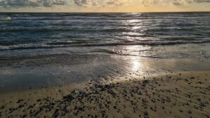 Une plage avec des vagues, un ciel dégagé et le soleil.