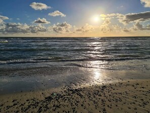 A beach with waves, a clear sky, and the sun.