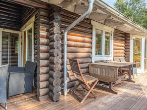 A log cabin with a wooden deck, a dining table with chairs, and a window.