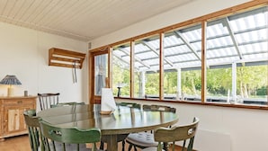 Une table de salle à manger ronde en bois, accompagnée de six chaises, un buffet en bois et une fenêtre avec un cadre en métal.