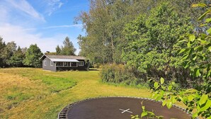 Une maison dotée d’un porche, entourée d’un champ verdoyant et d’une forêt dense.