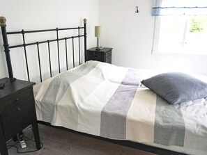 A bed with a striped bedspread, a bedside table with a lamp, and a window with a view of greenery. - 6 Person Holiday Home in Hallabro (Hallaröd)