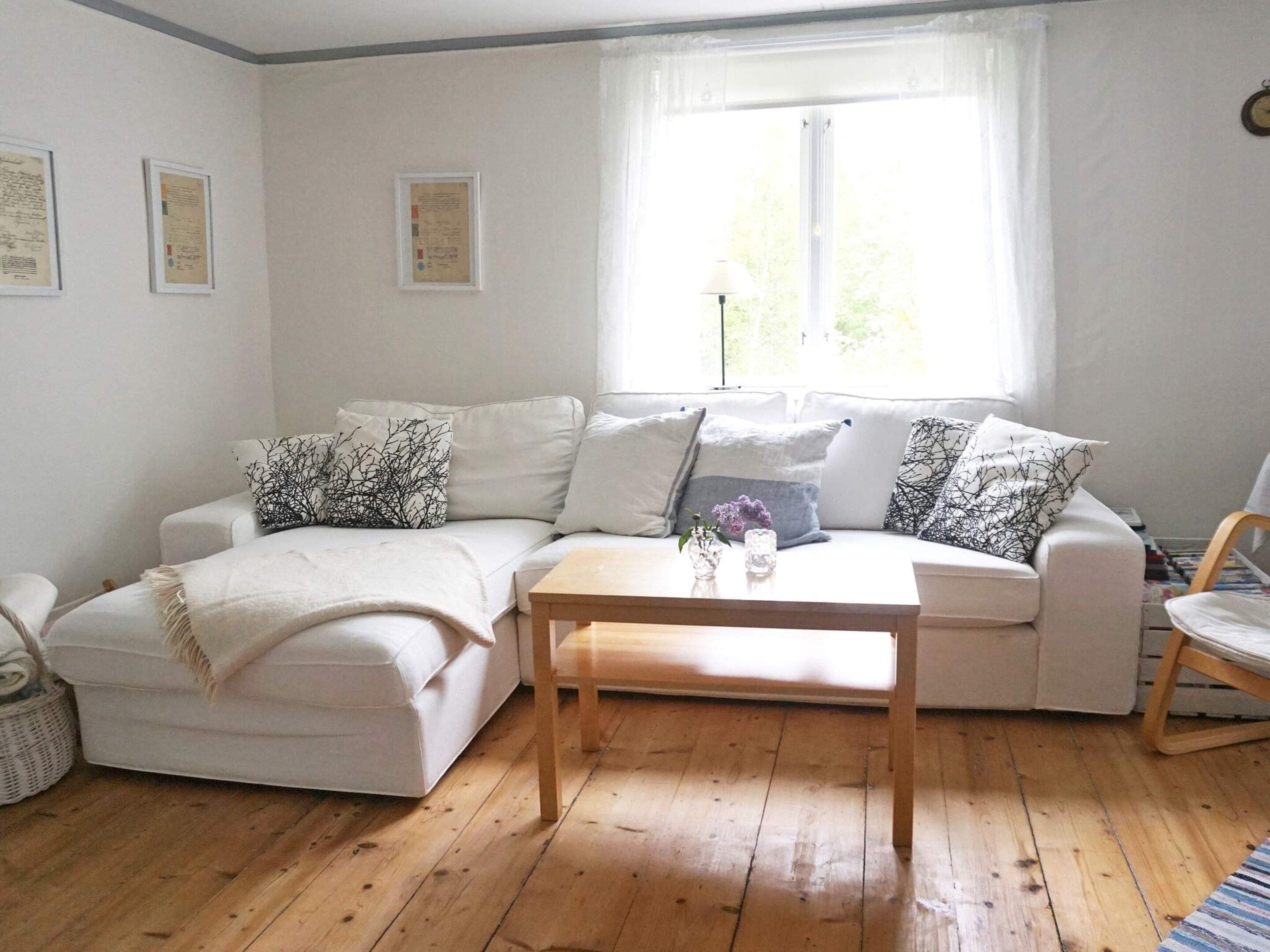 Una sala de estar con un sofá blanco, una mesa de centro de madera y un ventanal con cortinas.
