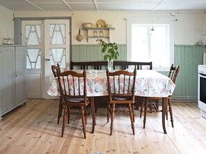 A dining area with a wooden table and chairs, a vase with a plant, and a kitchen in the background.
