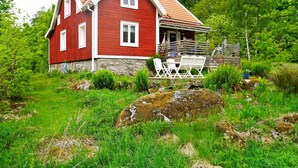 A red wooden house with a stone foundation, white windows, and a porch with outdoor furniture. - 6 Person Holiday Home in Hallabro (Hallaröd)
