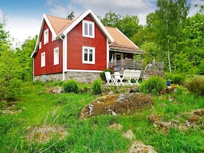 A red wooden house with a stone foundation, white windows, and a porch with outdoor furniture. - 6 Person Holiday Home in Hallabro-by Traum (Hallaröd)