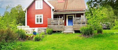 Une maison rouge avec un porche et une porte bleue, entourée d’une cour verdoyante et d’arbres.