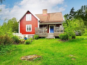 A red house with a porch and a blue door, surrounded by a grassy yard and trees. - 6 Person Holiday Home in Hallabro (Hallaröd)