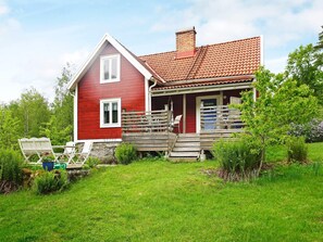 A red house with a tiled roof, a porch with wooden steps, and a grassy yard.