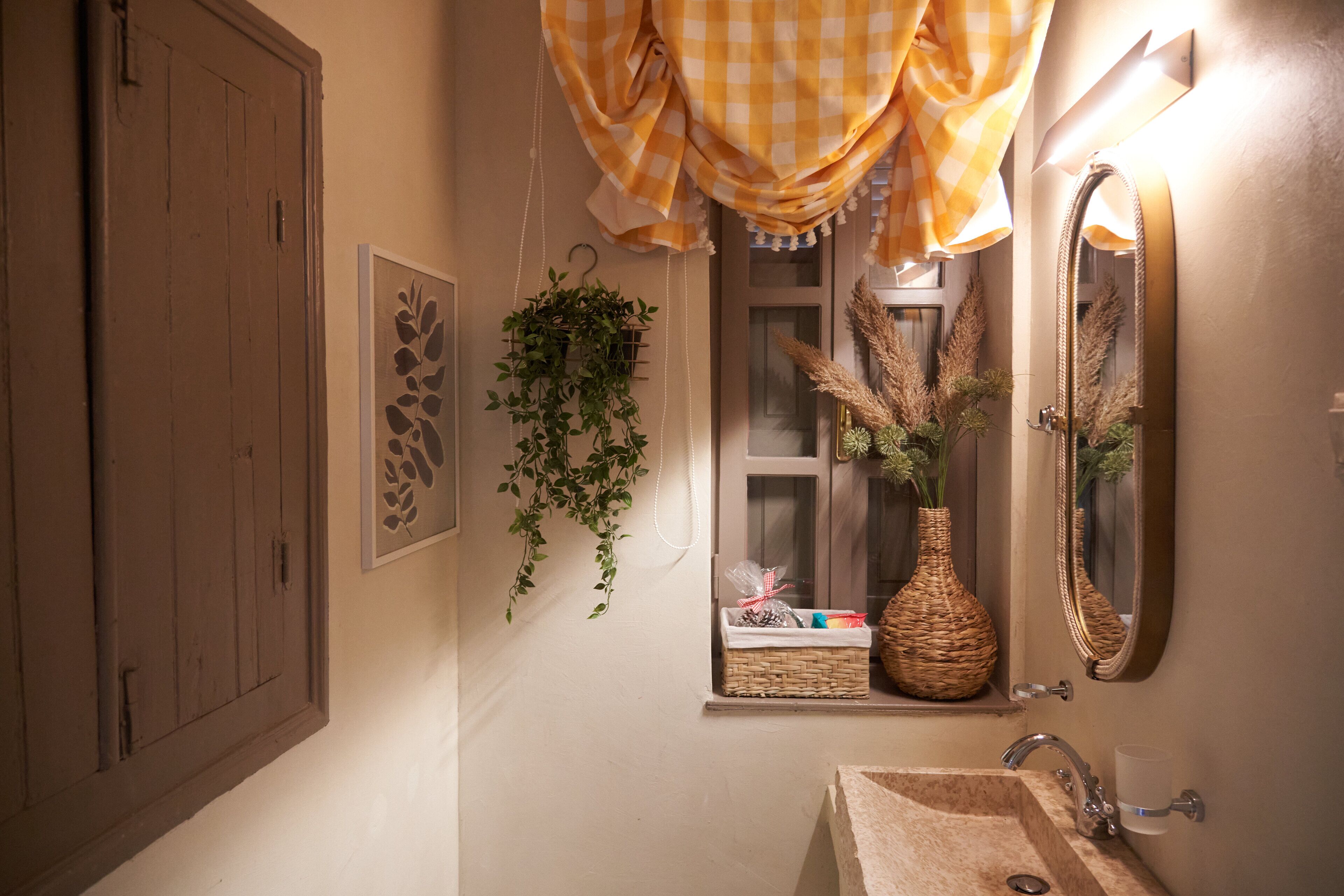 Un bagno con una porta di legno, una pianta pensile, un cesto di vimini, uno specchio e una finestra con vista all'esterno.