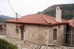 Un bâtiment en pierre avec un toit recouvert de tuiles, une antenne parabolique et une cheminée.