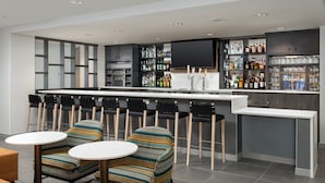 A modern bar area with a long counter, multiple stools, and a variety of liquor bottles. - SpringHill Suites by Marriott Cincinnati Mason (Mason)