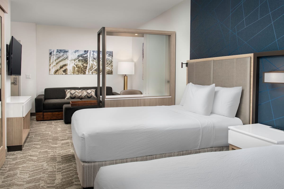 A hotel room with two beds, a sofa, a TV, a desk, and a large window.