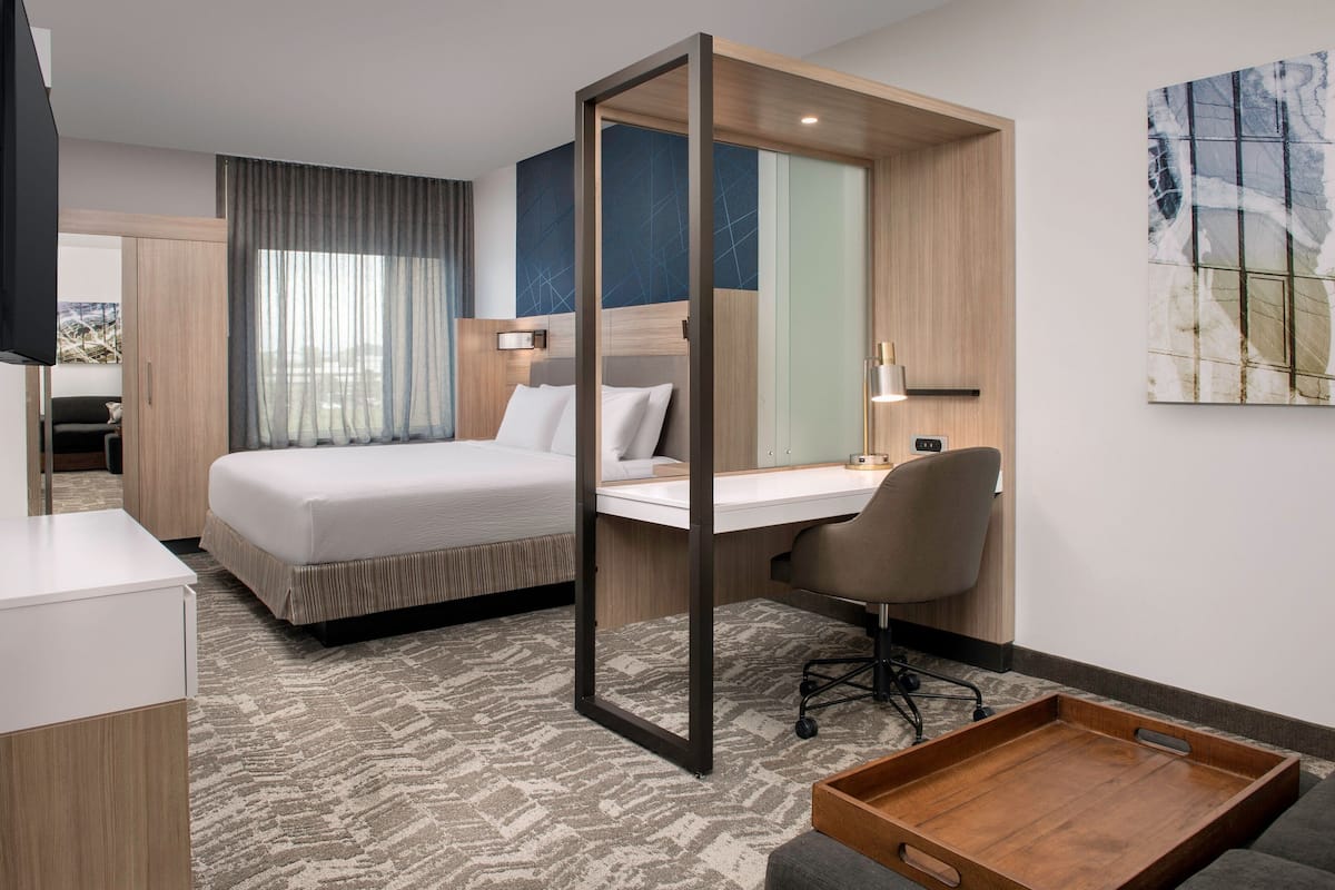A hotel room with a bed, desk, chair, and a wooden tray.