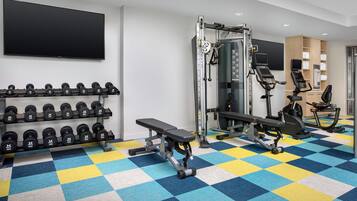 Un gimnasio con mancuernas, una banca, una máquina de pesas y una bicicleta estática.