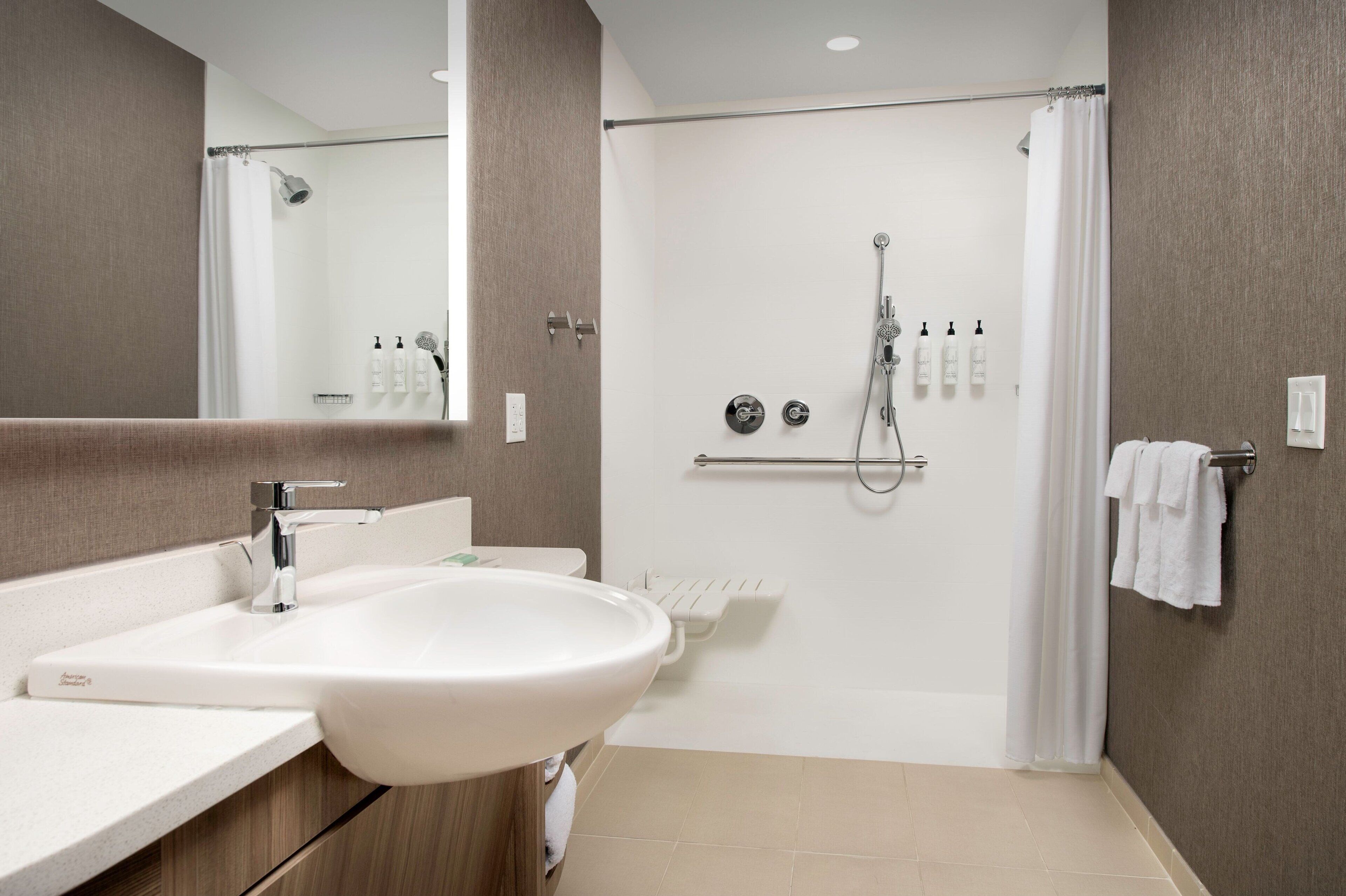 A modern bathroom with a white sink, mirror, shower, and towel rack.