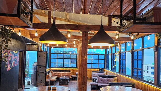 A rustic interior with wooden beams, pendant lighting, and large windows offering views. - The Hotel Nanglo (Taplejung)