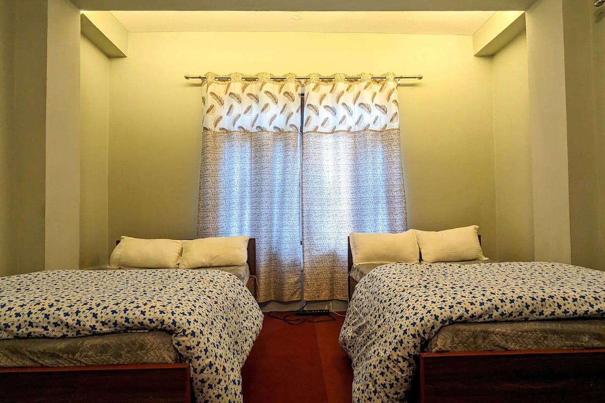 A room with two beds, a curtain, and a wall-mounted air conditioning unit.