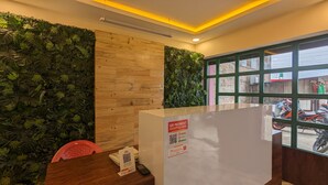 A reception desk with a QR code for payment, surrounded by a wooden panel and a green leafy wall. - The Hotel Nanglo (Taplejung)