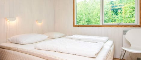 Quarto com cama, duas luminárias na parede, janela com vista para vegetação e uma cadeira branca.