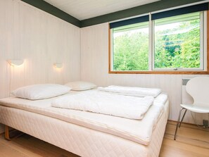 A bedroom with a bed, two wall-mounted lights, a window with a view of greenery, and a white chair.