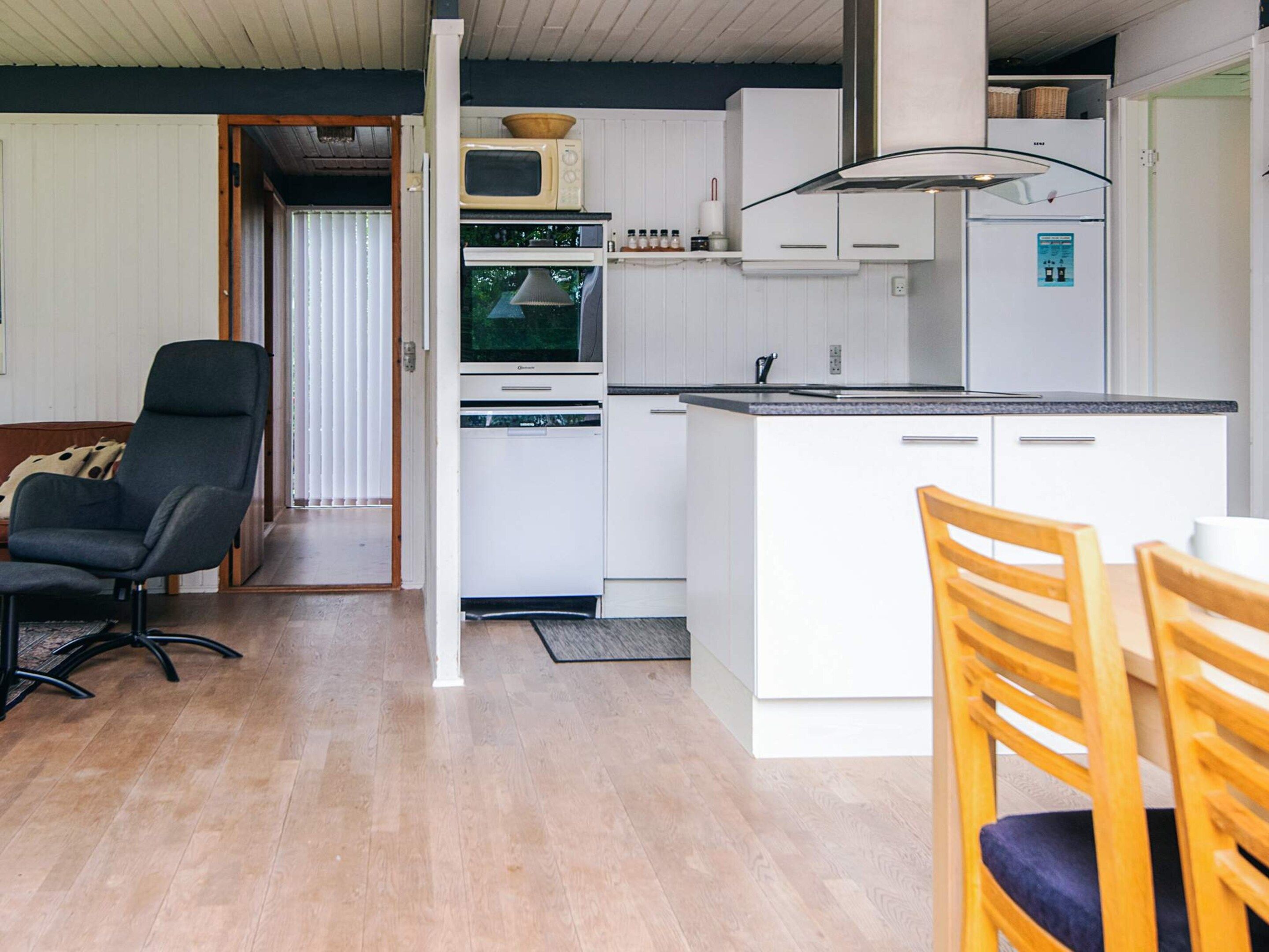 A compact kitchen with white cabinetry, a microwave, a stove, and a refrigerator. There is a dining area with a table and two chairs.