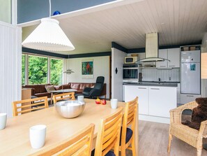 Una cucina moderna con mobili bianchi, un forno a microonde e un frigorifero. C'è un'area pranzo con un tavolo e sedie in legno, e un divano sullo sfondo.