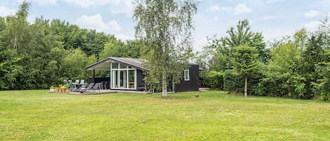 Une maison moderne avec une grande façade vitrée, une terrasse dotée de mobilier d’extérieur et une pelouse bien entretenue.