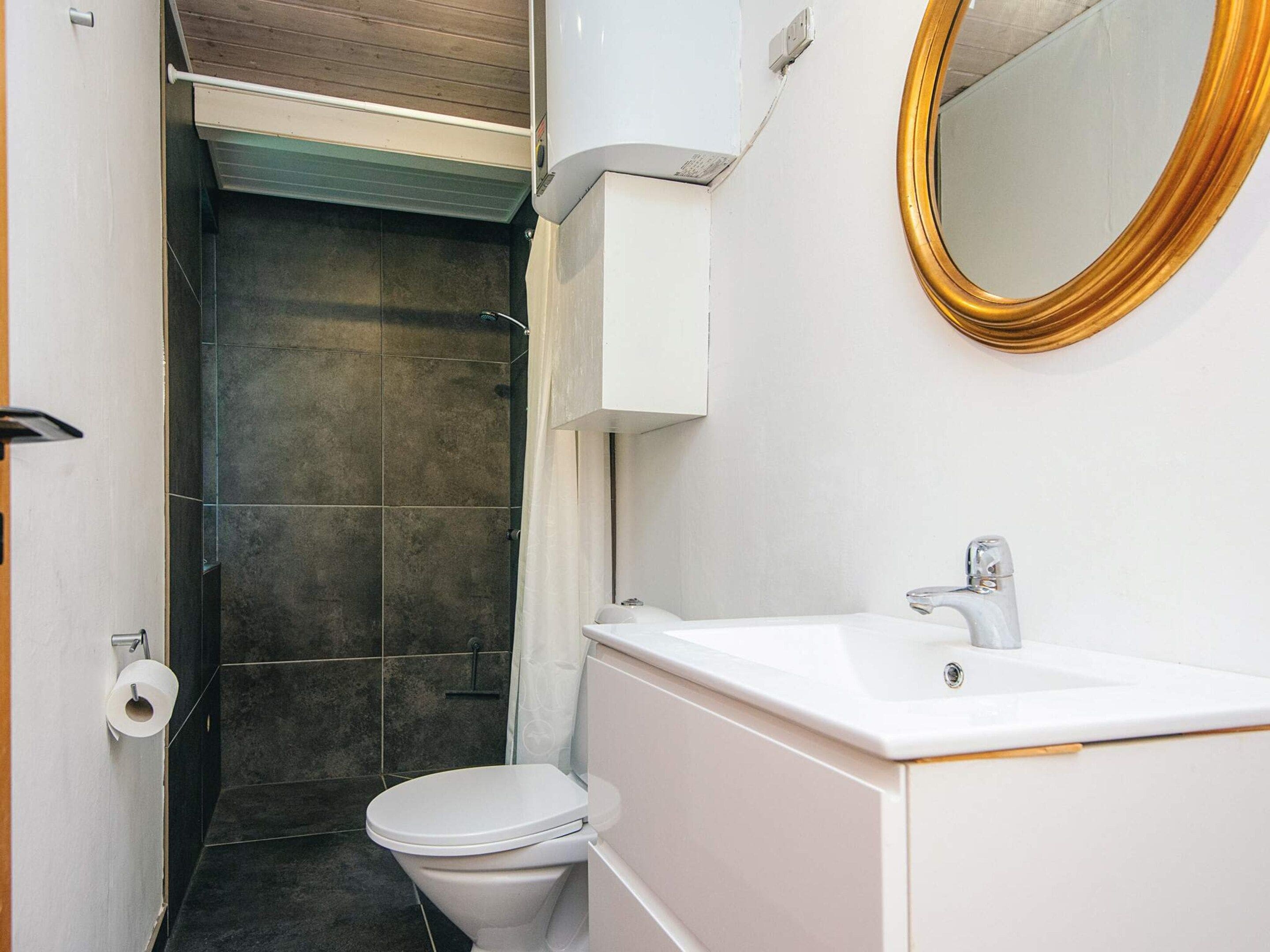 A bathroom with a white toilet, a sink, and a mirror with a gold frame.