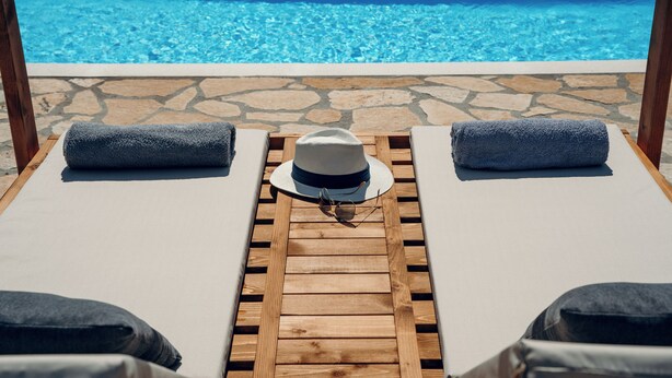 Eine Holzterrasse mit zwei Liegestühlen, einem Hut und einer Sonnenbrille auf der Sitzfläche.
