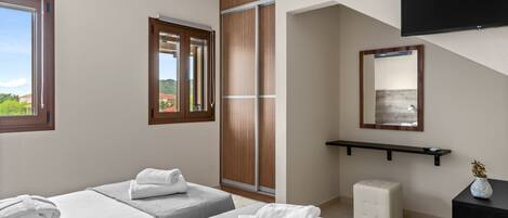 Quarto de hotel com duas camas, uma janela grande, uma porta deslizante, televisão montada e uma mesinha com um vaso.