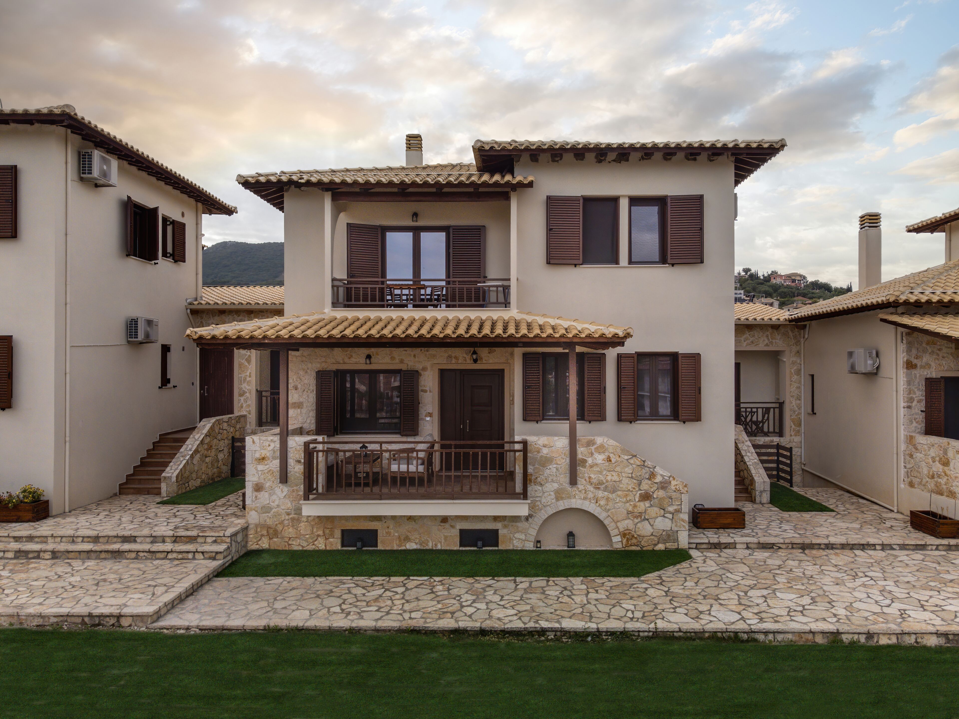A two-story house with a stone facade, a balcony, and a stone staircase leading to the entrance.