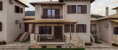 A two-story house with a stone facade, a balcony, and a stone staircase leading to the entrance.