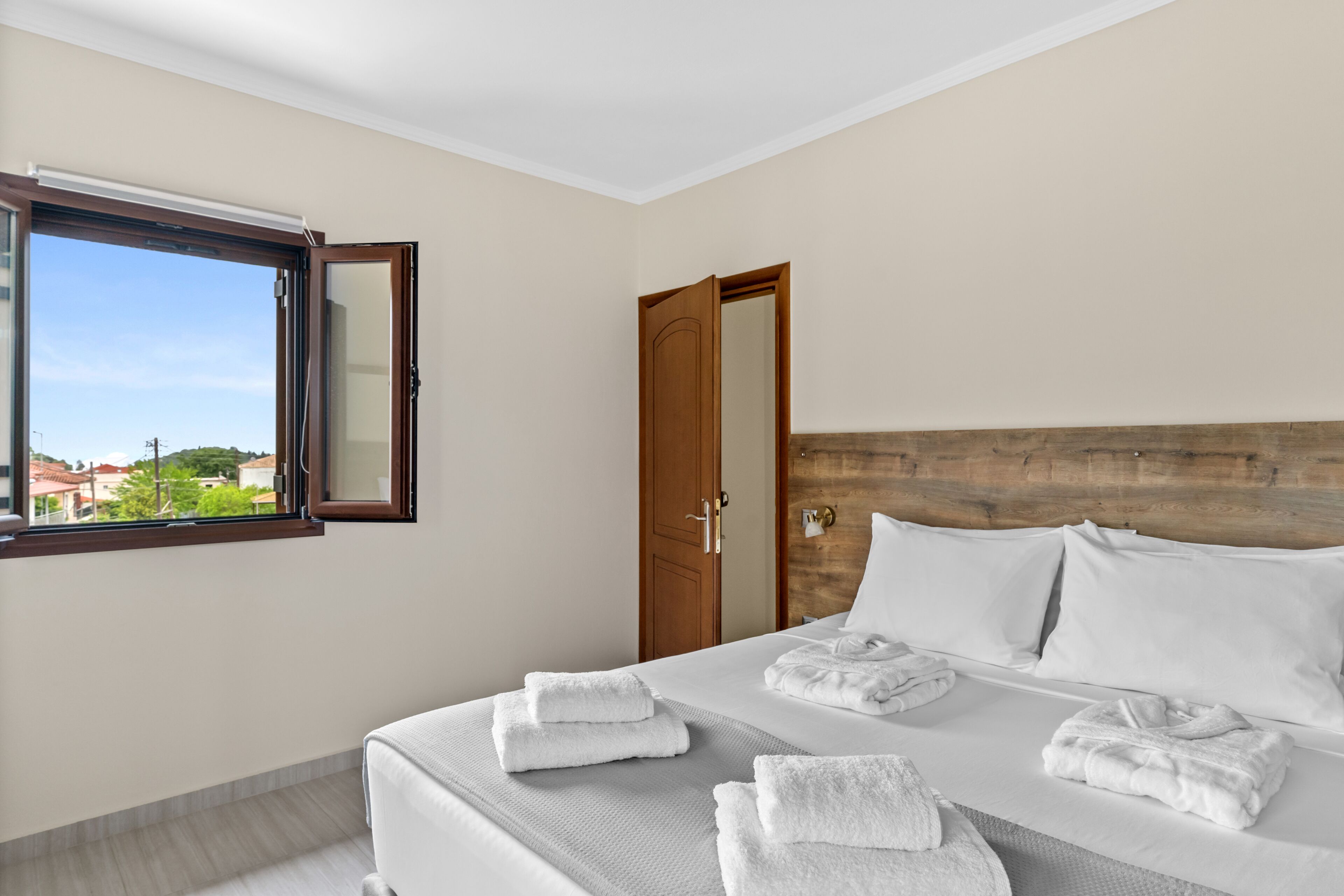 Ein Hotelzimmer mit Bett, Handtüchern, einem Holzkopfende, einem Fenster mit Blick und einer Tür.