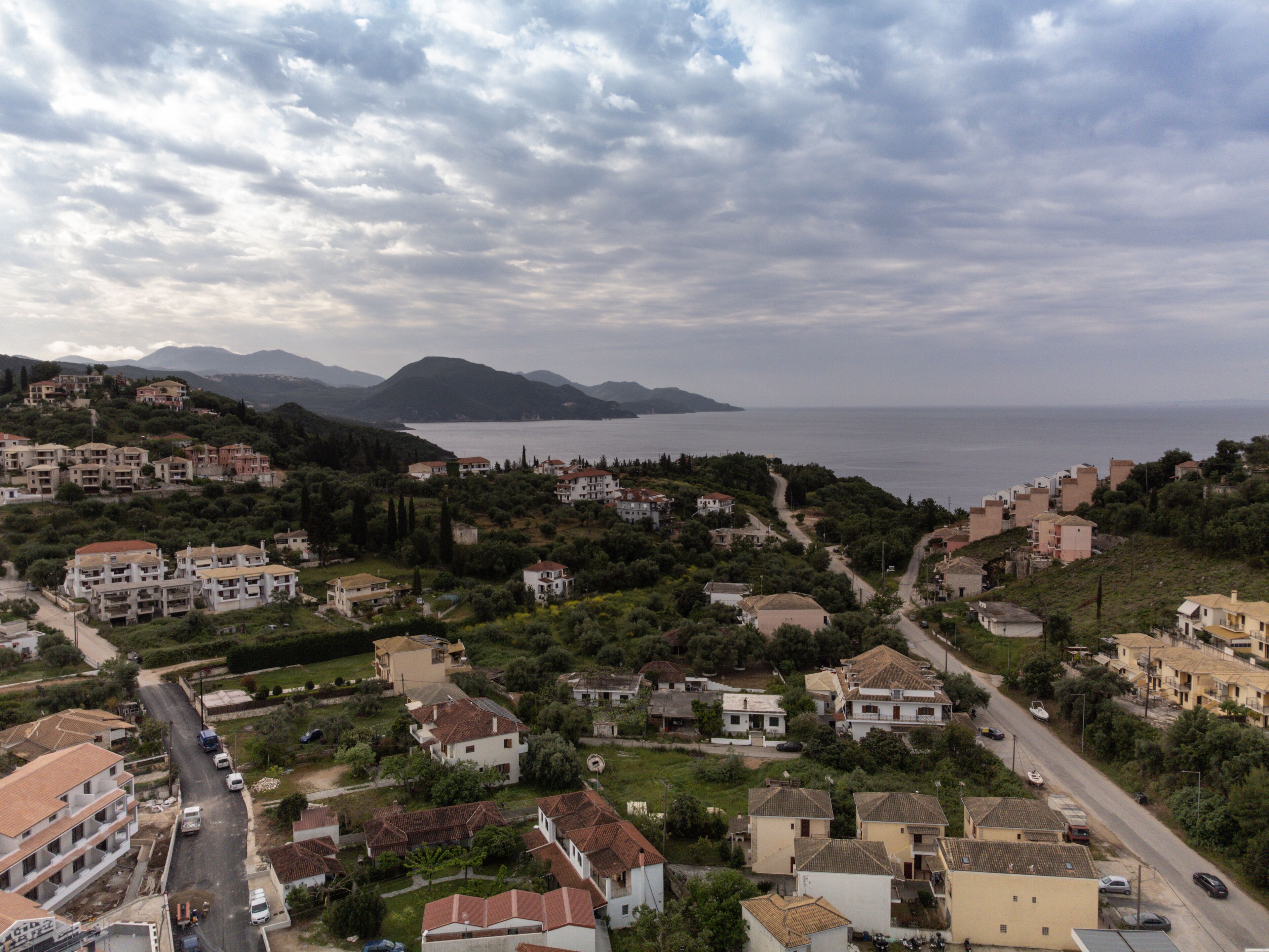 Un pueblo costero con edificios residenciales, calles y vistas al mar y montañas al fondo.