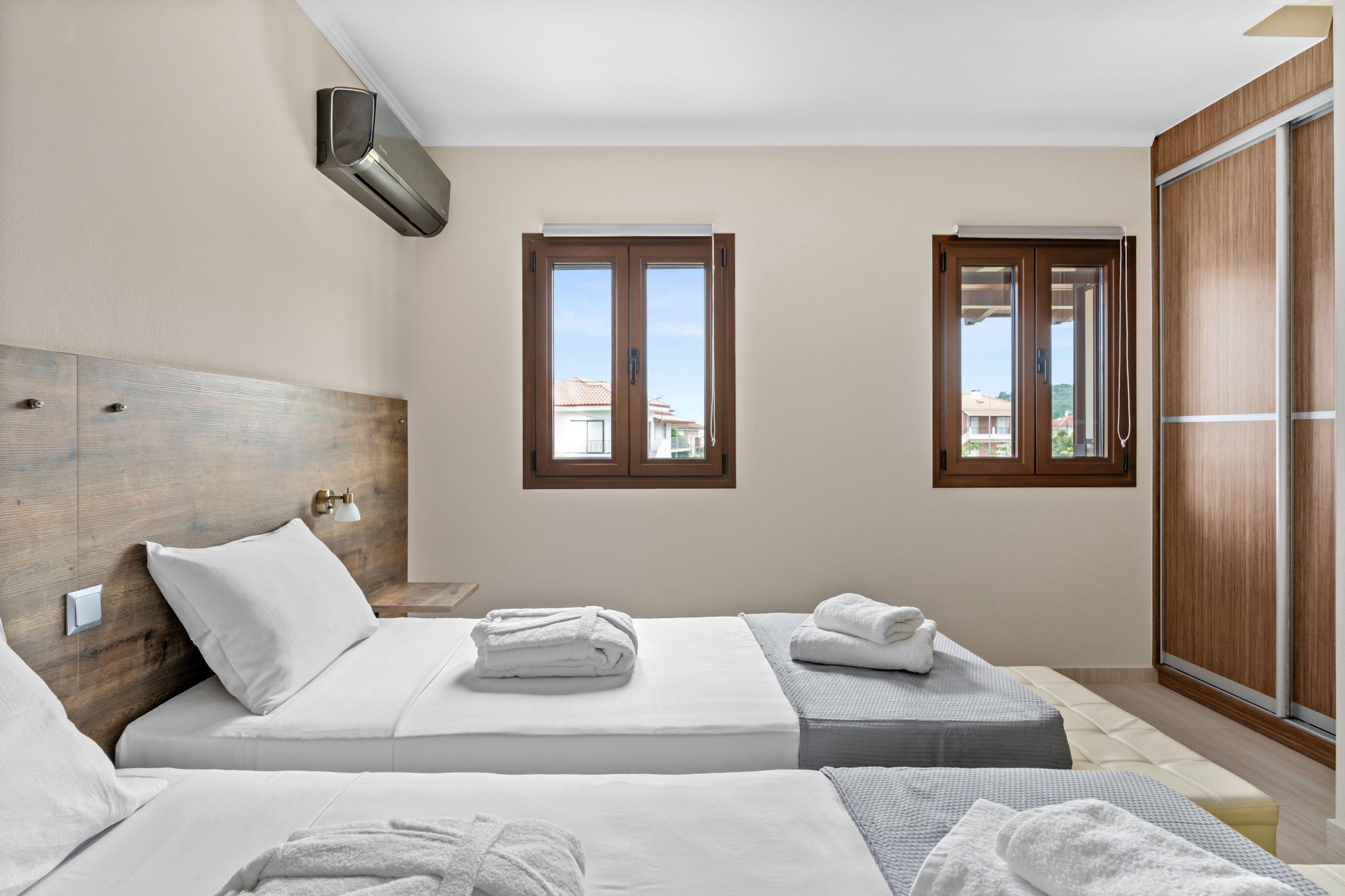 Habitación de hotel con dos camas, cabecero de madera, ventana y puerta corredera.