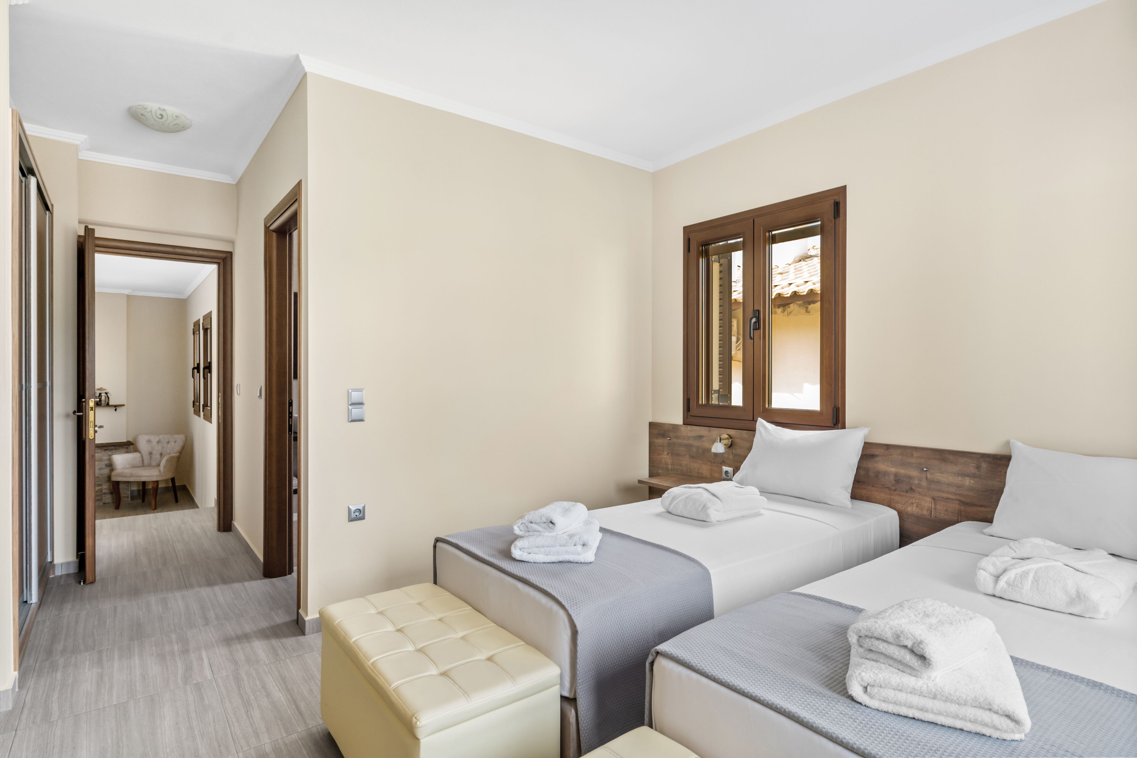 Une chambre d’hôtel avec deux lits, une tête de lit en bois, une fenêtre donnant sur un beau paysage et une salle de bain visible par une porte ouverte.