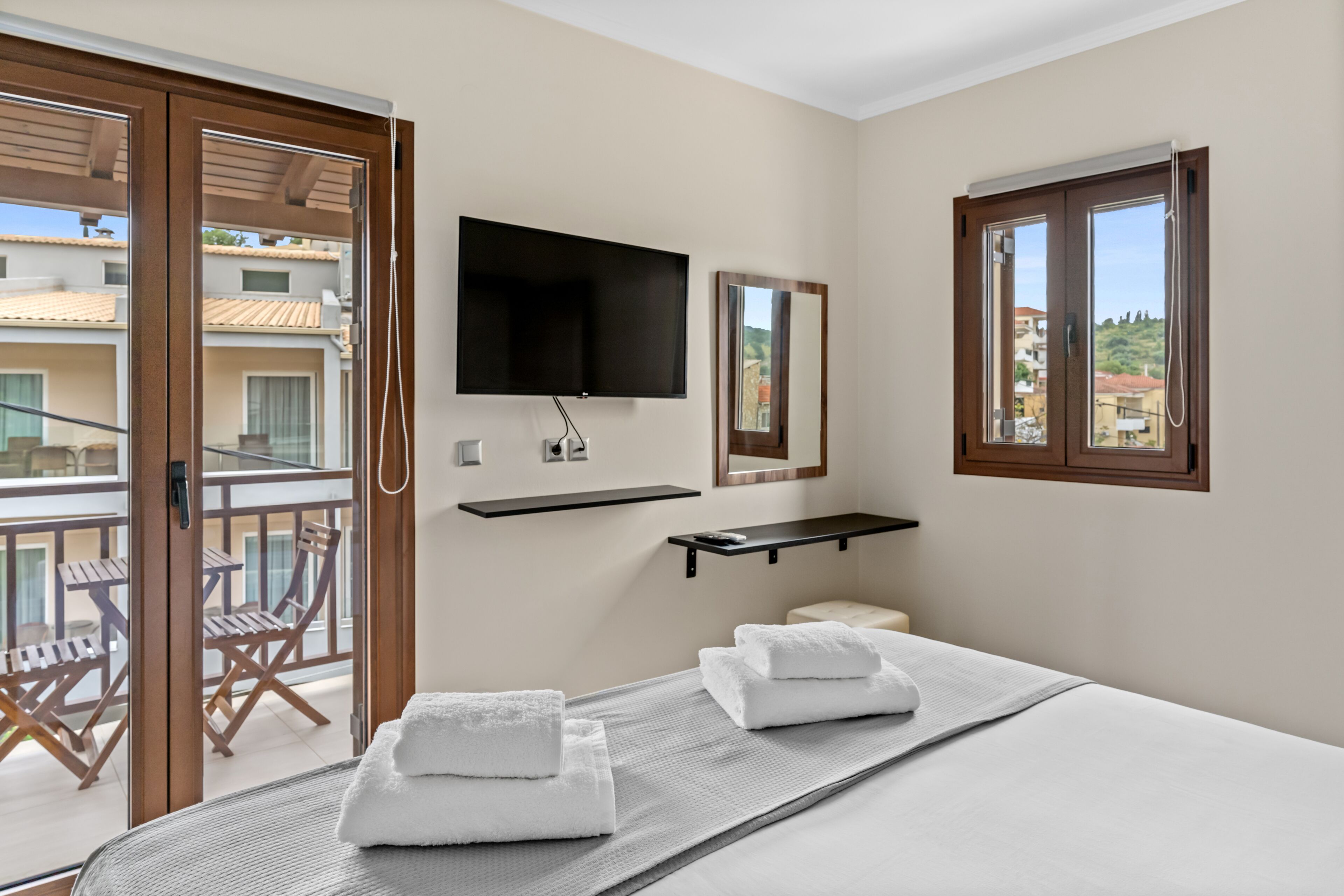 A hotel room with a bed, a TV mounted on the wall, a window, and a balcony with chairs.