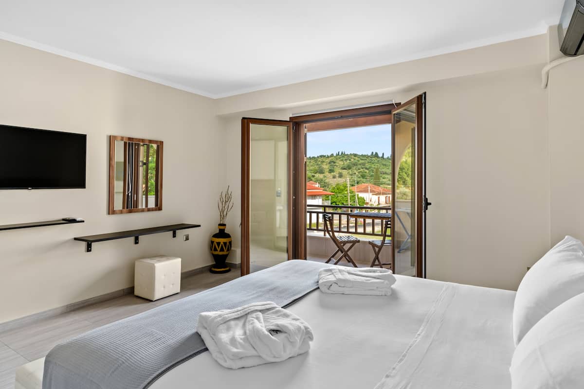 Une chambre d’hôtel avec un lit, une télévision, une petite table et un balcon donnant sur les collines.