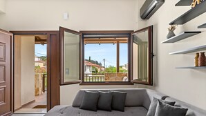 Ein modernes Wohnzimmer mit einem grauen Ecksofa, einem Holztisch und einem großen Fenster mit Blick auf die Nachbarschaft.