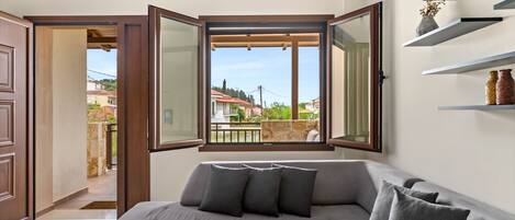 Uma sala de estar moderna com um sofá seccional cinza, uma mesa de centro de madeira e uma janela grande com vista para o bairro.