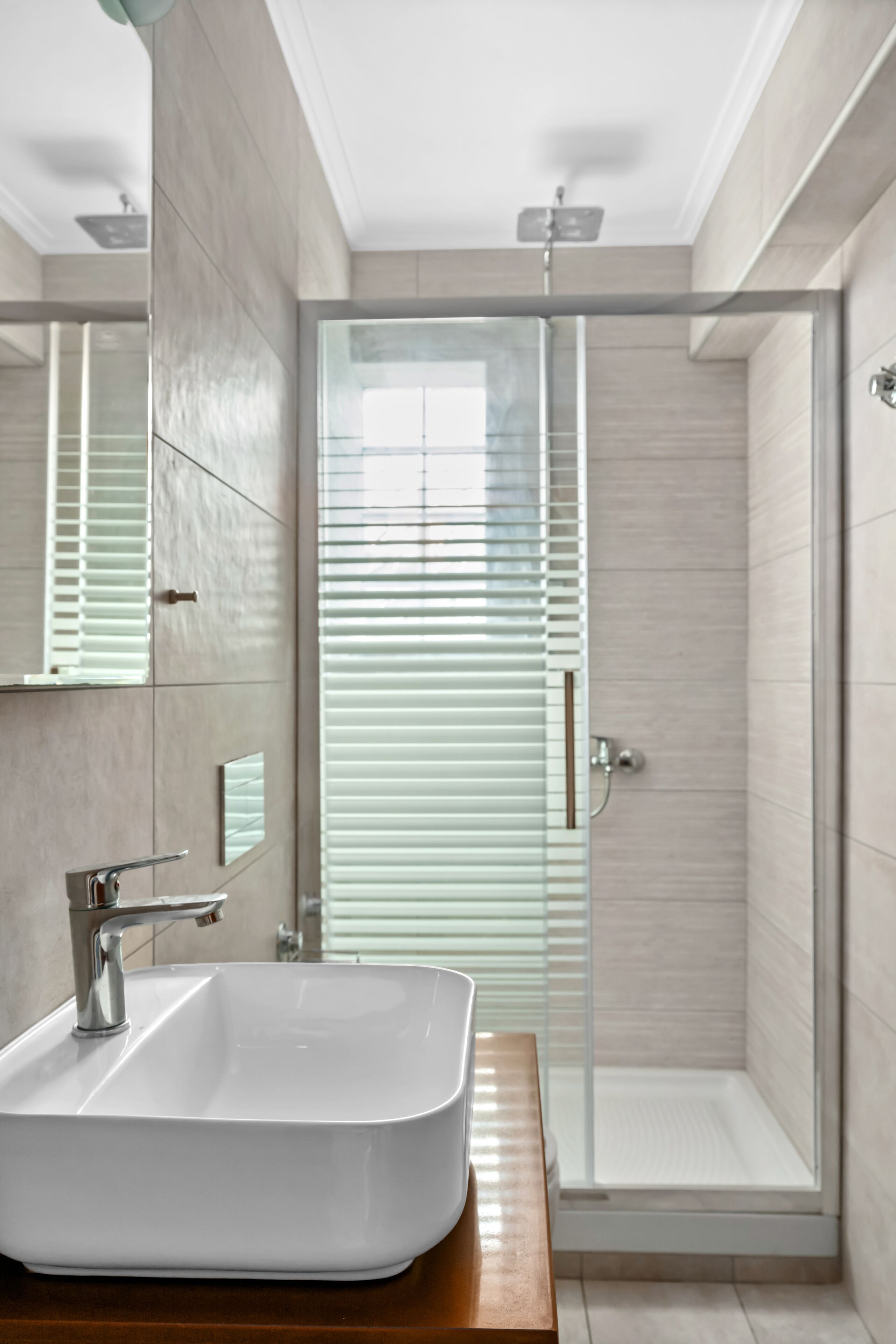 A modern bathroom with a large white sink, a mirror, and a glass-enclosed shower.