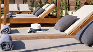 Eine Holzterrasse mit Liegestühlen, einem Hut und einer Sonnenbrille auf einem der Stühle.
